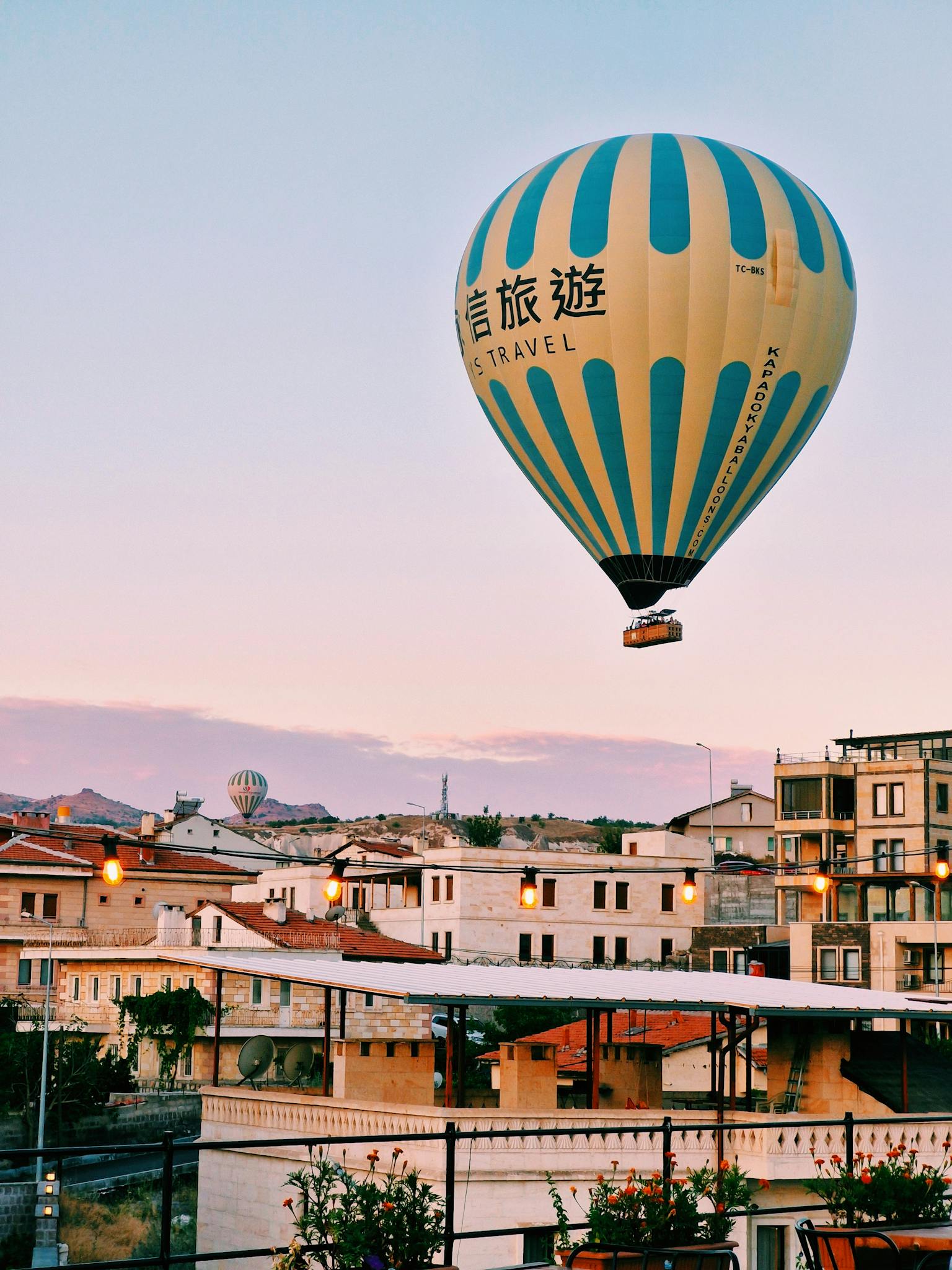 A vibrant hot air balloon soars over Cappadocia's traditional landscape during a stunning sunset.
